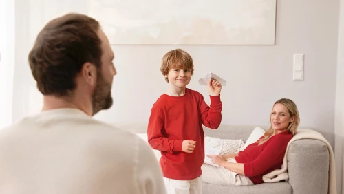 Für Ei Electronics konzipierte und produzierte Albert Bauer Amazon Premium A+ Content. Glückliche Familie sitzt im Wohnzimmer, das Kind wirft einen Papierflieger